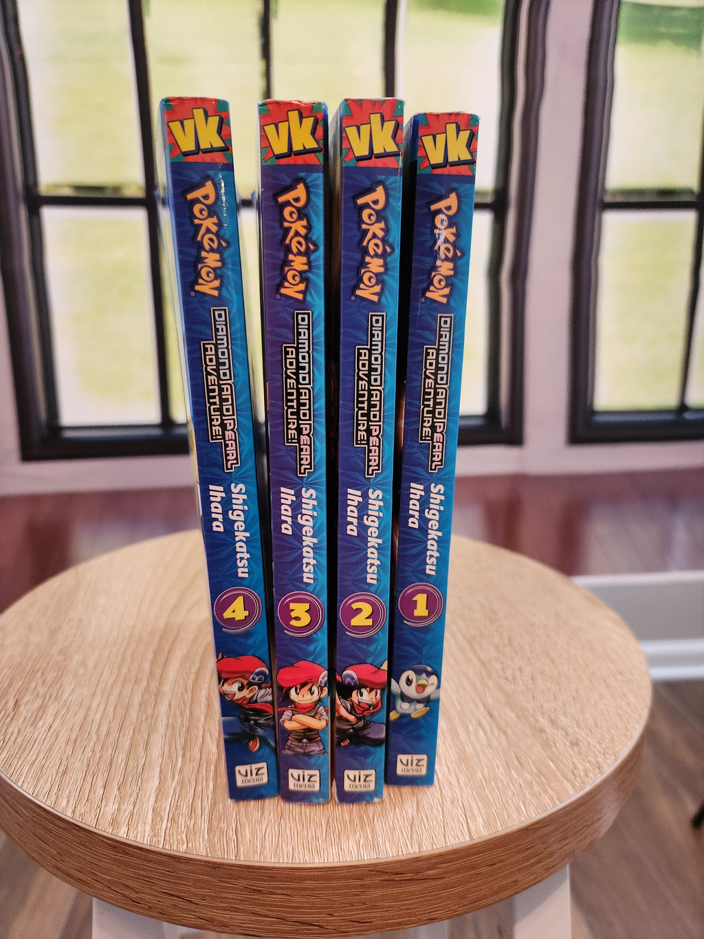 Four Pokémon books stacked on a wooden surface with a colorful background