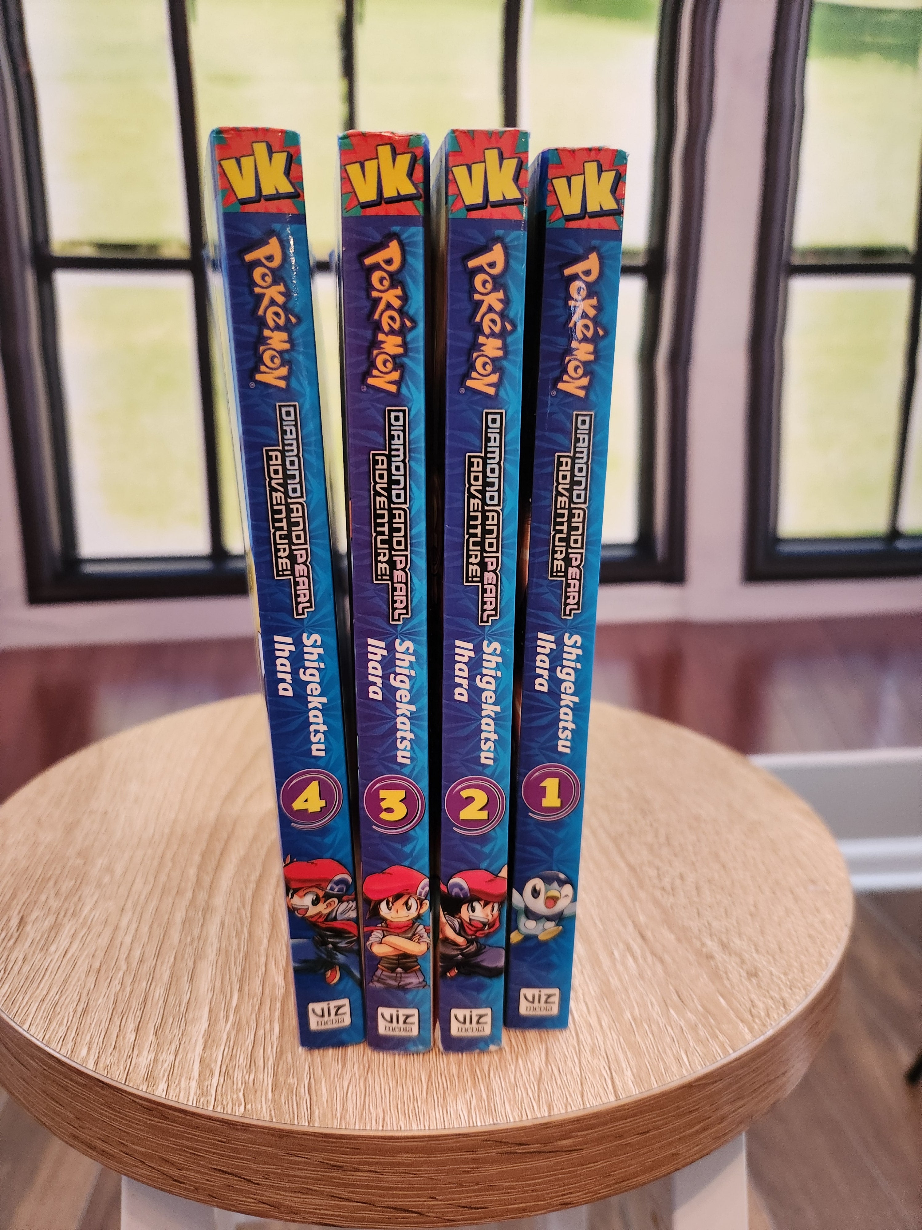 Four Pokémon books stacked on a wooden surface with a colorful background